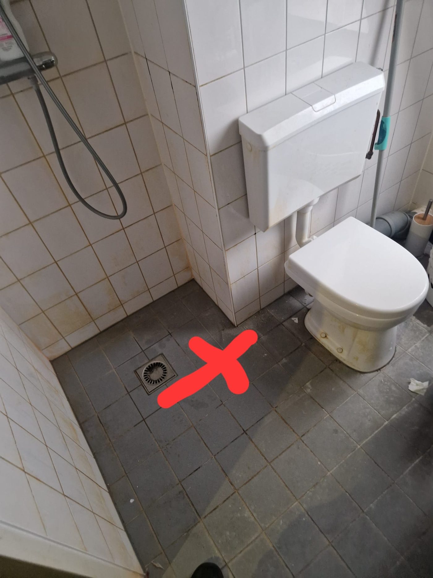 Lekkage bij het doucheputje in een betegelde badkamer, leklocatie gemarkeerd met een rood kruis